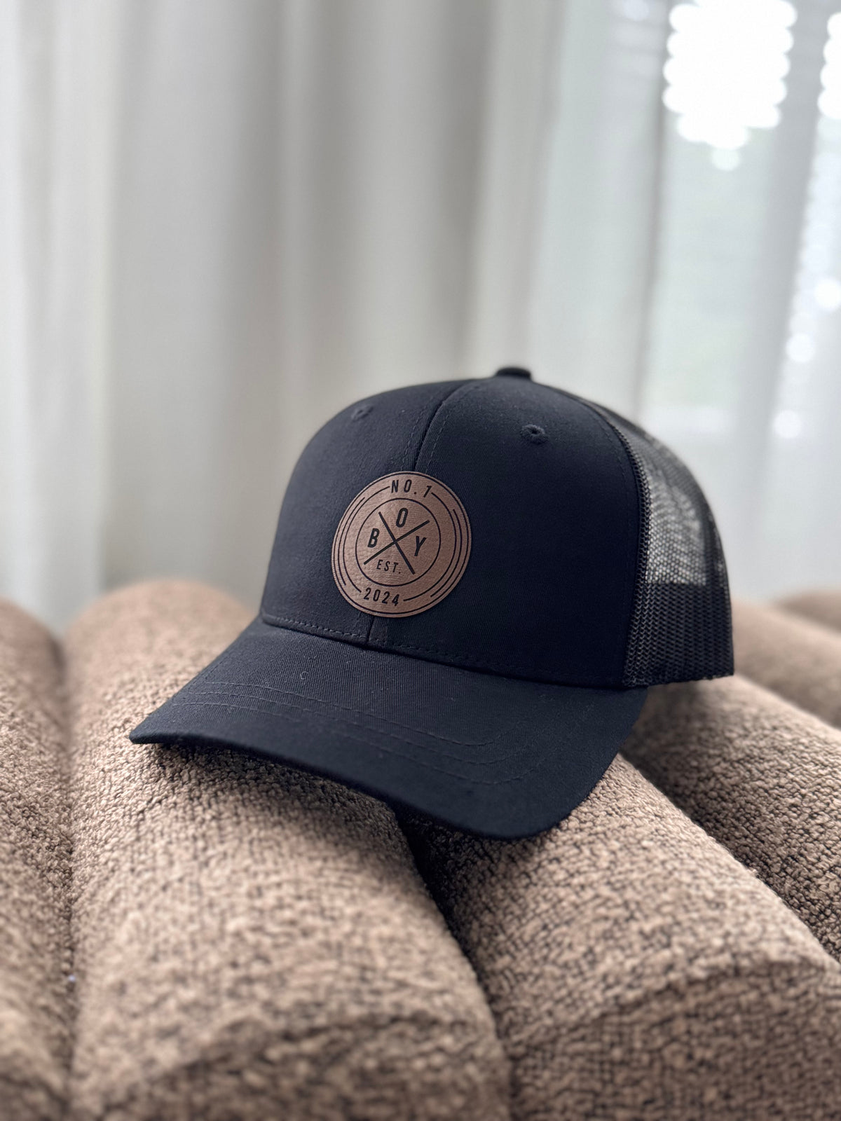 Musta lasten trucker-lippalakki ruskealla pyöreällä nahkajäljitelmämerkillä.
