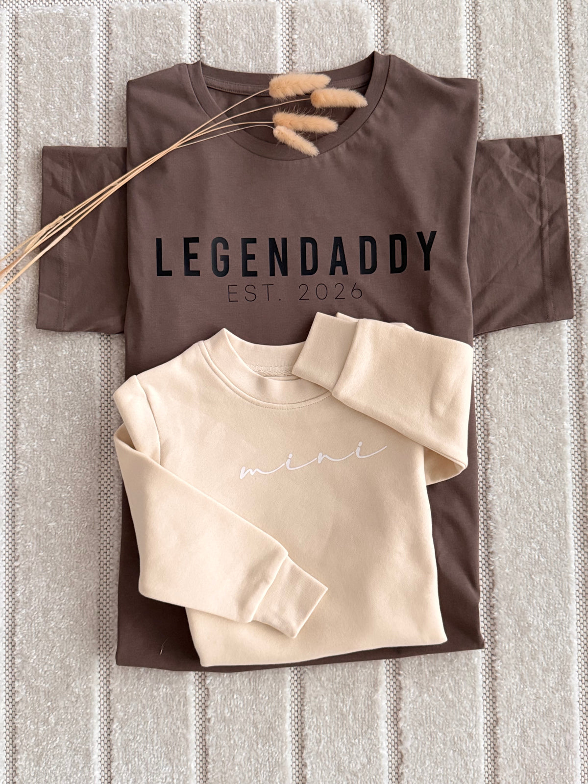 A styled flat-lay of two sweatshirts on a textured gray knit blanket.
